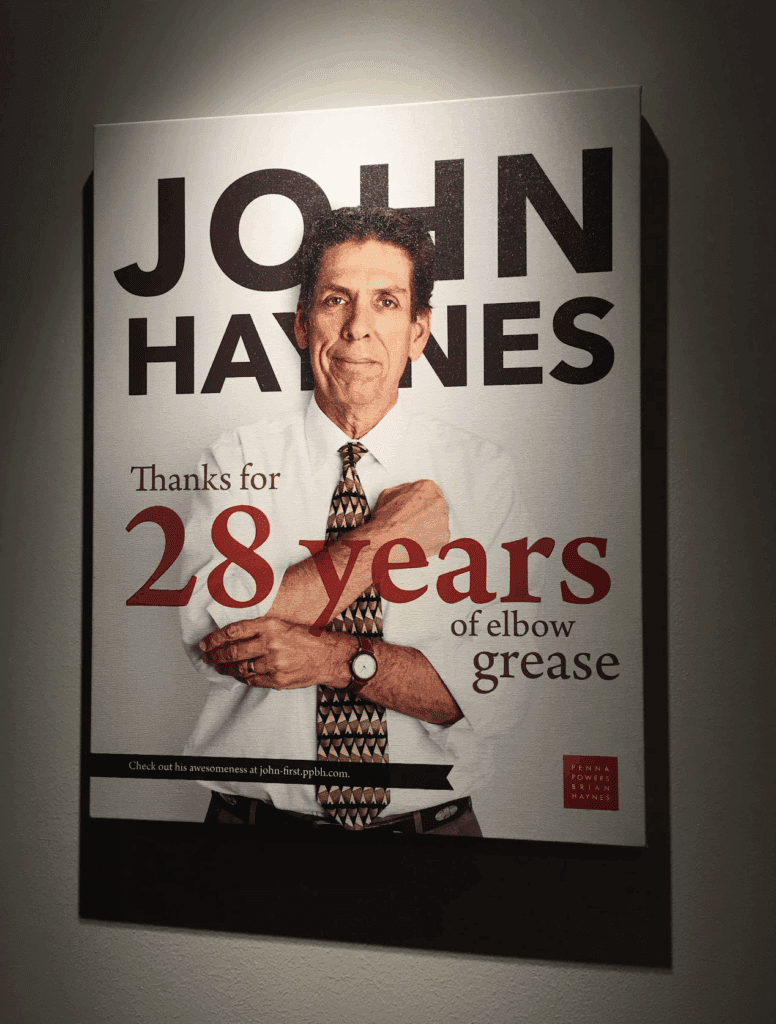 Poster celebrating John Haynes's 28 years of service at Penna Powers Brian Haynes, featured on a wall to honor his decades of work.