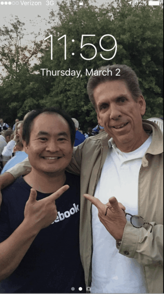 iPhone lock screen screenshot featuring John Haynes and Dennis Yu from a 2015 photo at an outdoor event in Salt Lake City