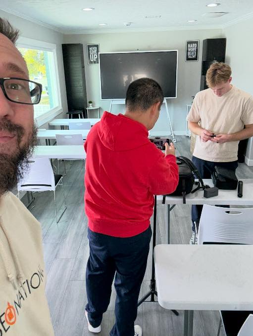 Damon Burton, Dennis Yu, and Sam McLeod setting up in Damon’s training room — the same white tables and Hard Work Beats Talent posters
