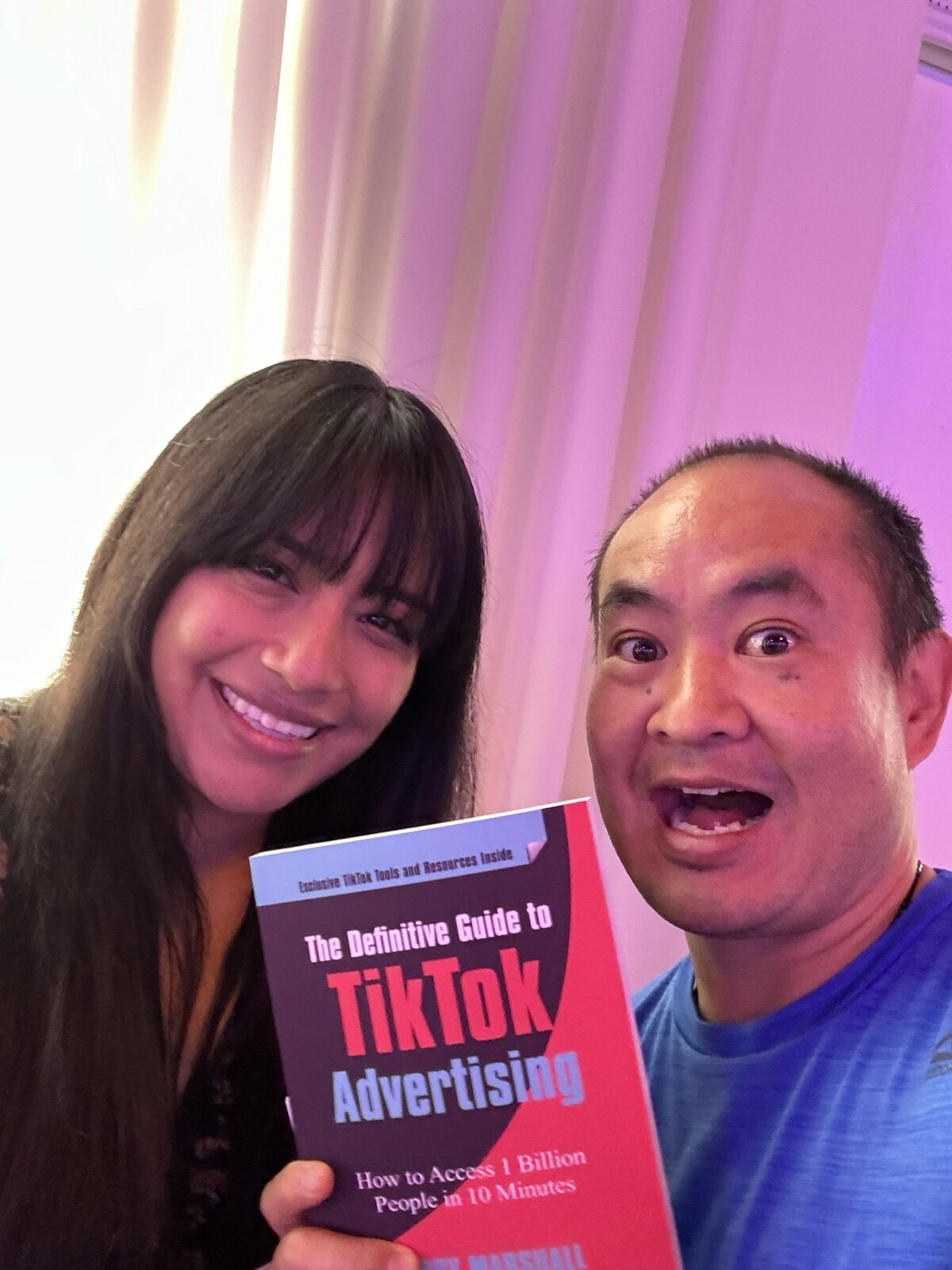 Dennis Yu and a woman holding the TikTok advertising book under pink conference lighting