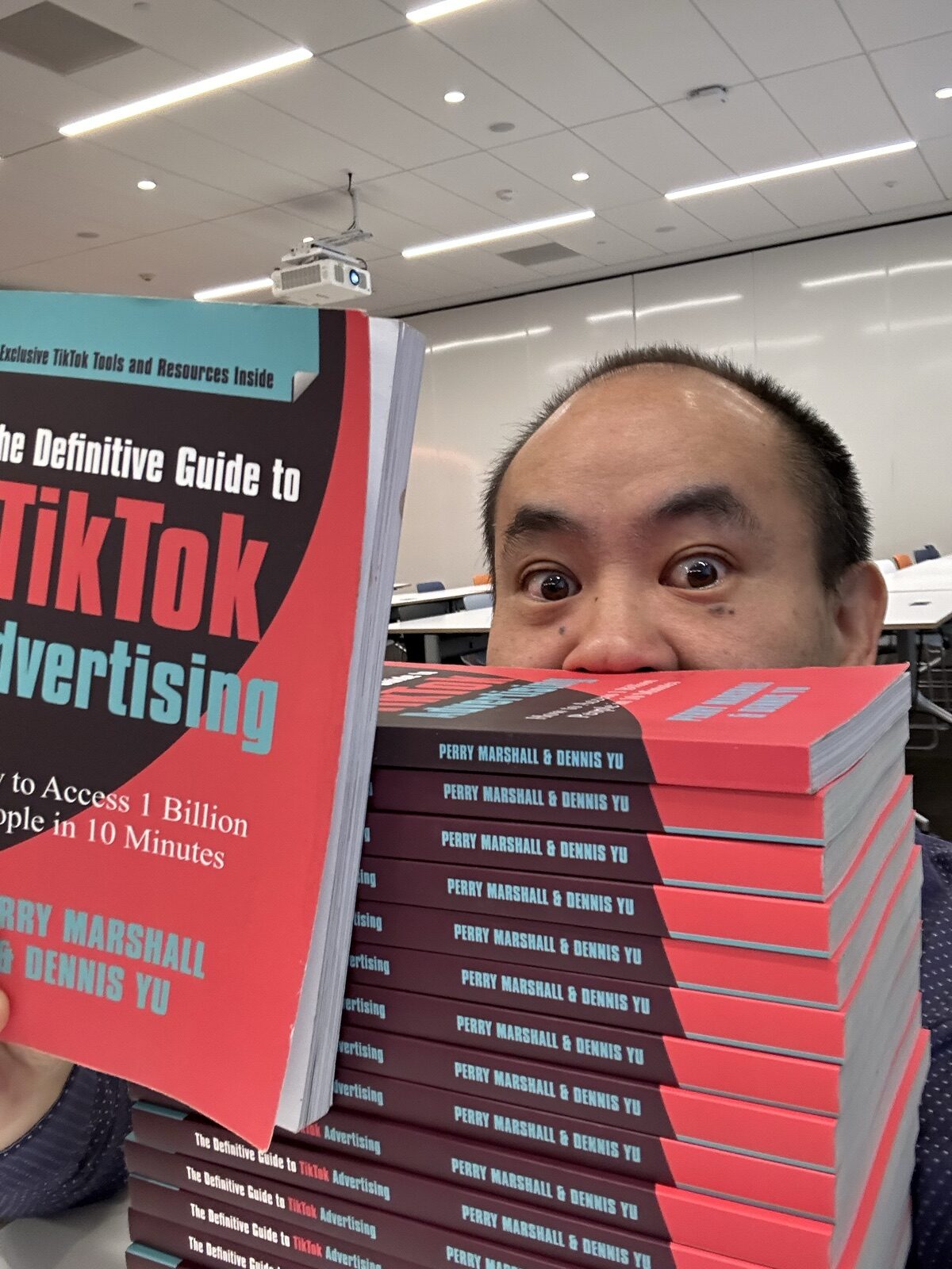 Dennis Yu peeking over a stack of TikTok advertising paperbacks in a conference room