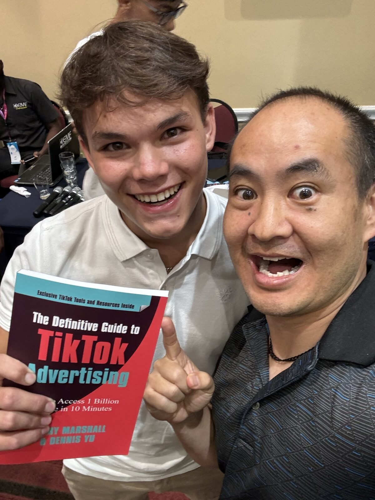Two men at a conference table with mics, holding the TikTok advertising book