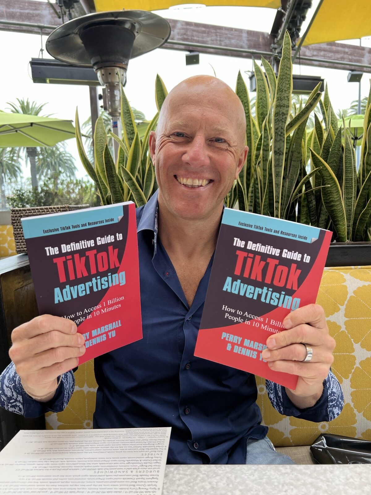 Man at a patio table holding two copies of the TikTok advertising book