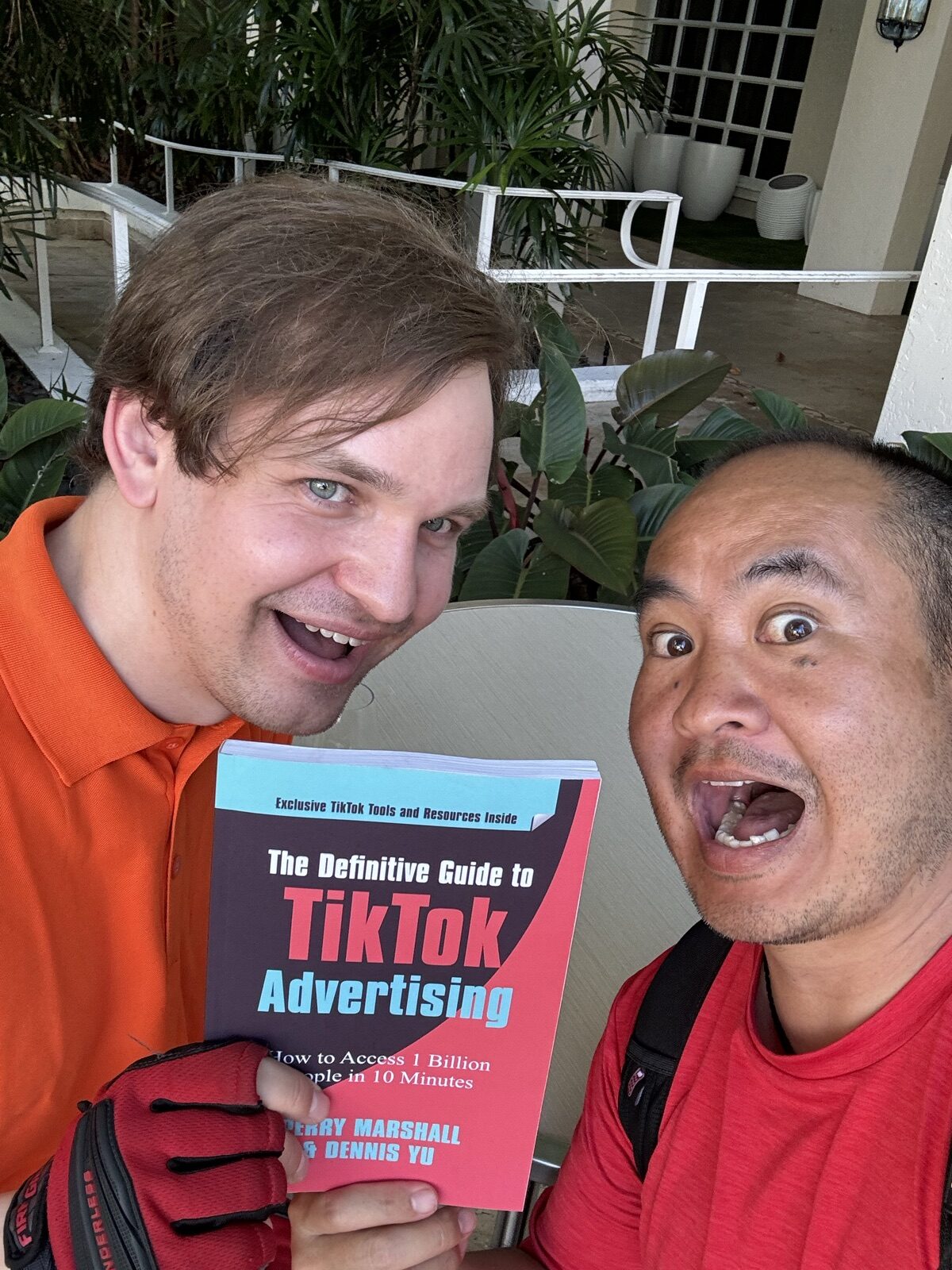 Dennis Yu and a man in an orange polo holding The Definitive Guide to TikTok Advertising outdoors