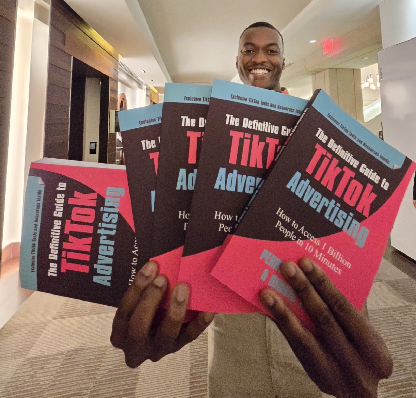 Young man in a conference hallway holding five copies of the TikTok advertising book
