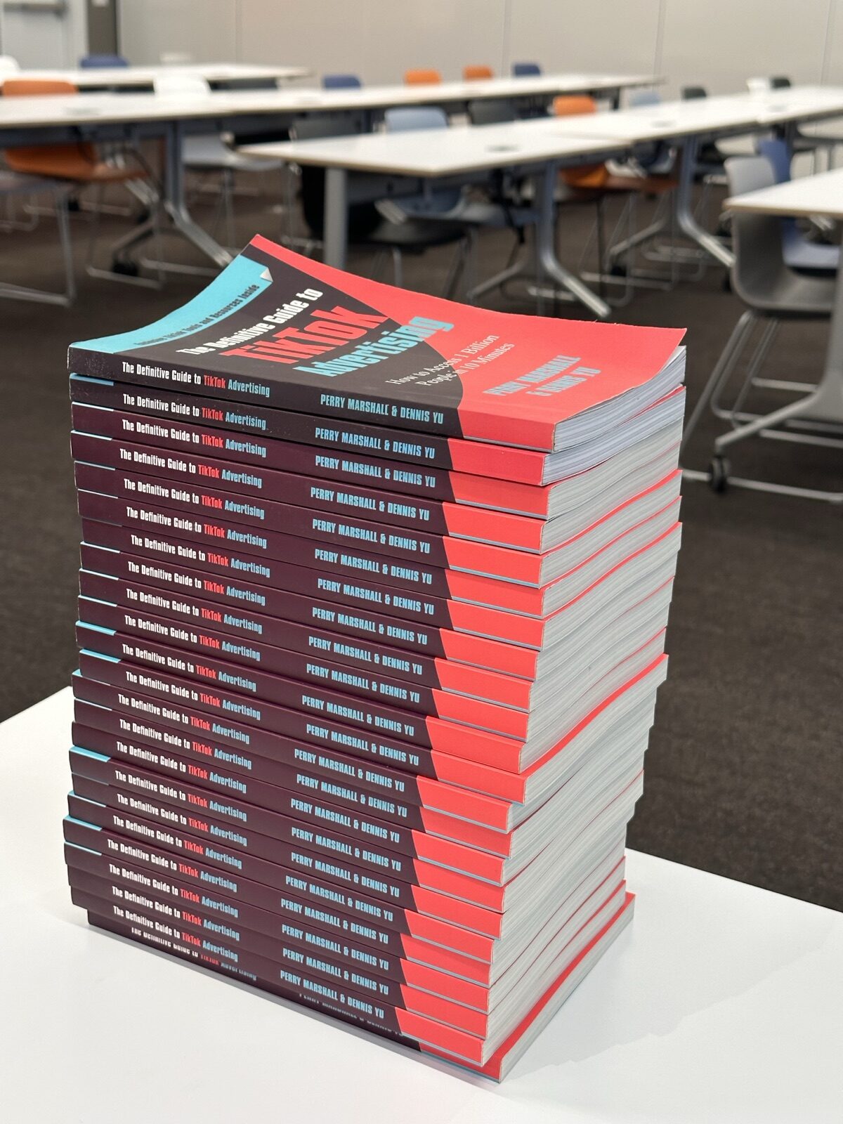 Tall stack of The Definitive Guide to TikTok Advertising on a table in an empty conference room