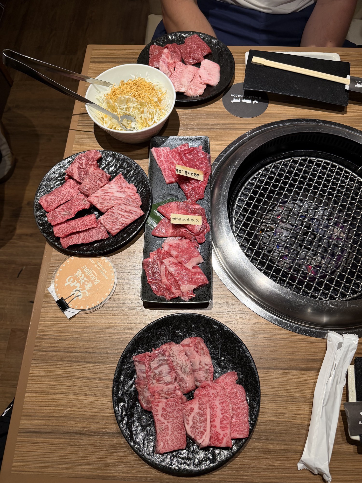 Meatings in Tokyo: Why I Love to EEAT With Good Friends 1 Full table at Yakiniku Black Hole Shinjuku 3-chome with branded wagyu plates, cabbage salad, Black Hole coaster, and a built-in charcoal grill