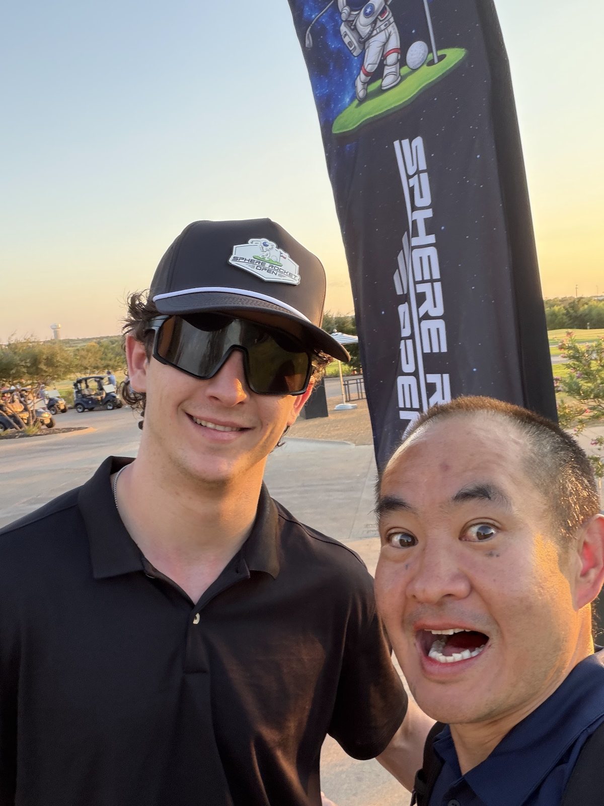 Dennis Yu and Jack Allard next to the Sphere Rocket Open flag at sunset