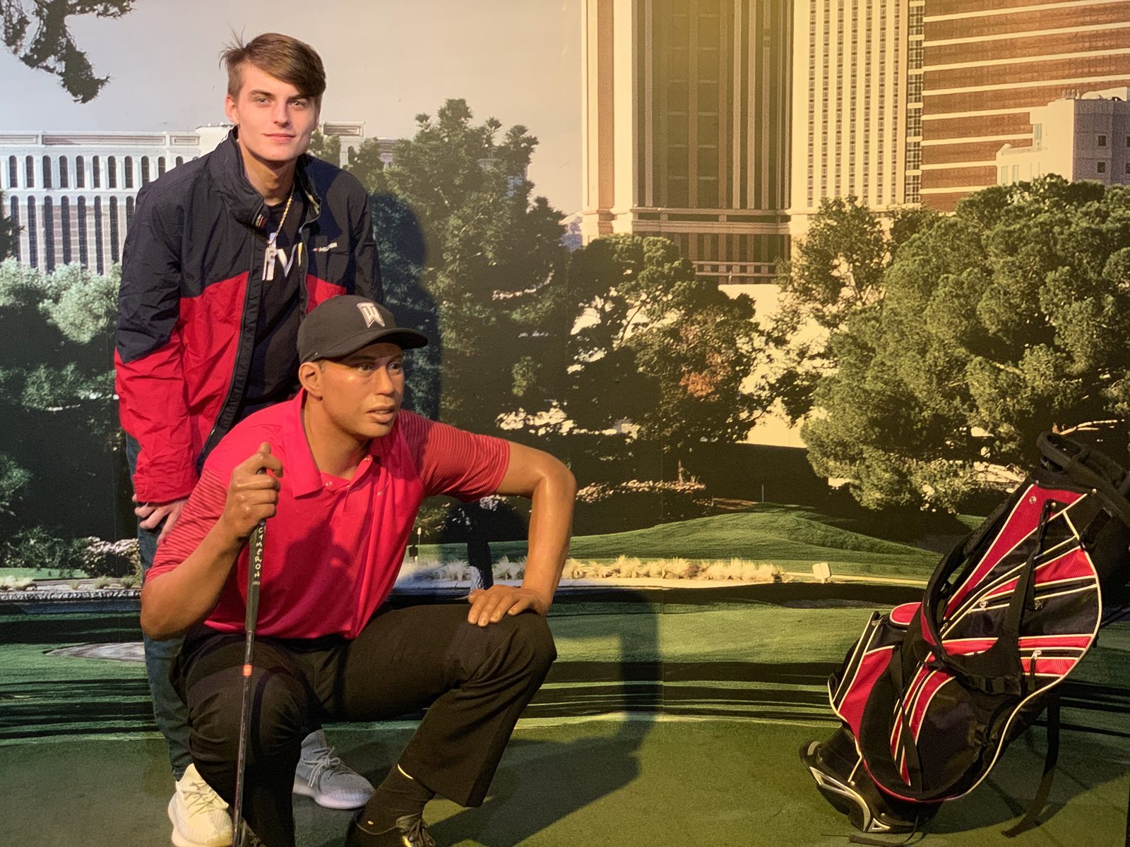 Dennis Yu in a red polo doing the Tiger pose at a golf photo wall, October 2019