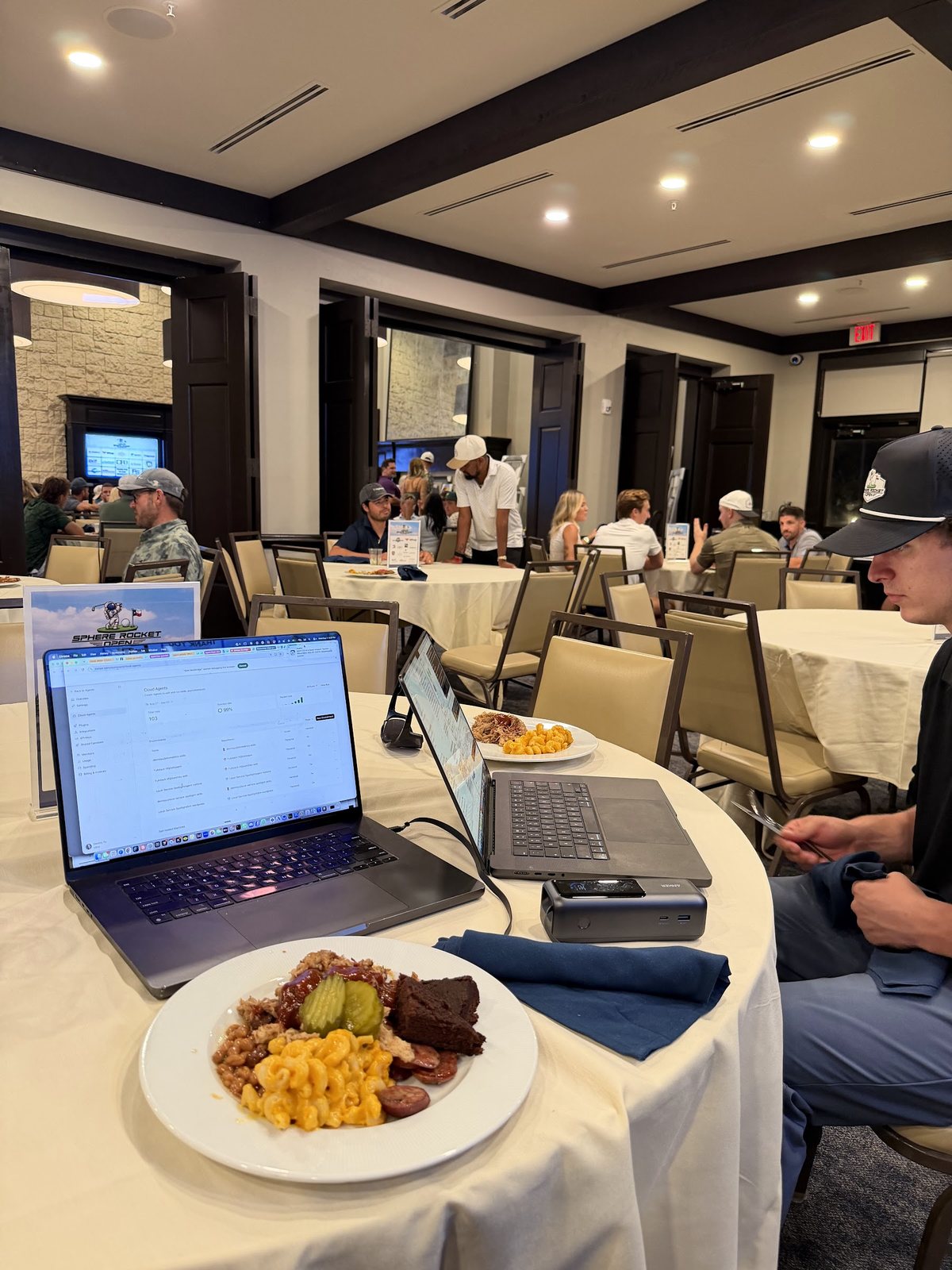 A laptop running AI agents next to a plate of Texas barbecue at the Sphere Rocket Open