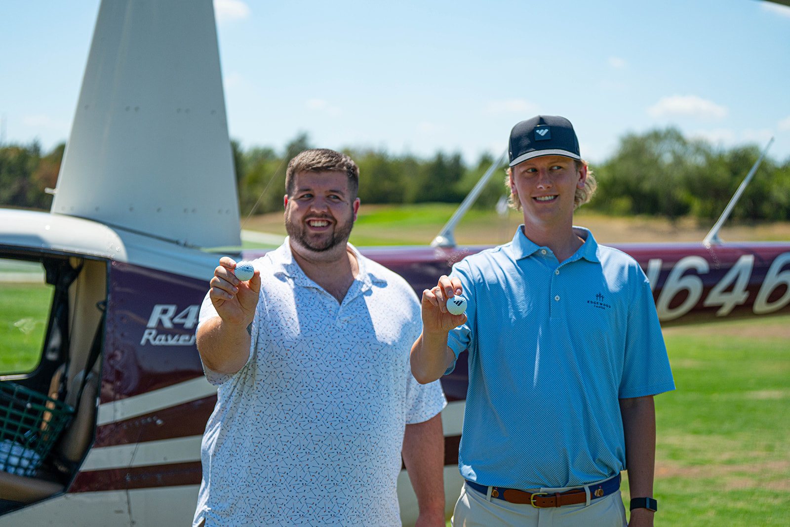 Justin Nelson and Aden Trano holding golf balls in front of an R44 helicopter before the ball drop